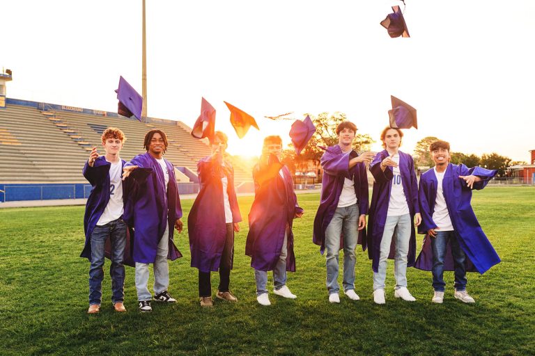 high school seniors in cap and gowns posing on school soccer field