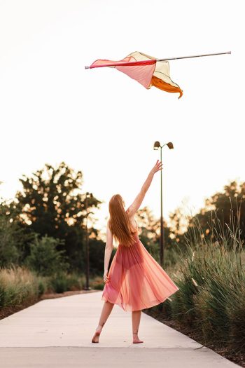 high school senior color guard member spinning her flag at sunset in a natural environment