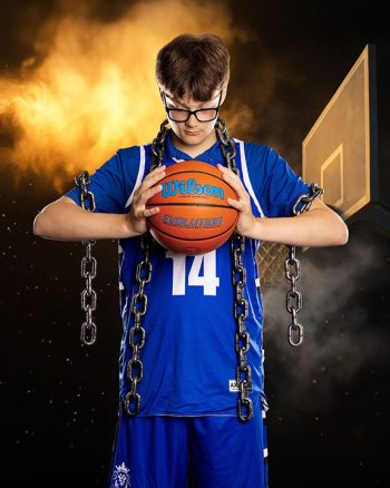 high school boy basketball player portrait put on a smoke filled digital backdrop. player is holding the ball and wearing chains to demonstrate strength.