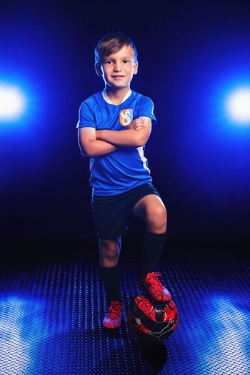 young boy soccer player posing with his foot on the ball, taken in the bc visuals bartow, florida studio using blue smoke and lights