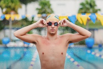 swim team media day featuring a male swimmer at the pool wearing swim cap and goggles