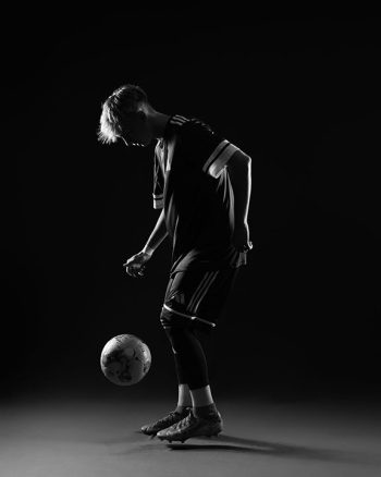 auburndale high school soccer player dribbling the soccer ball on a simple black studio background with rim light