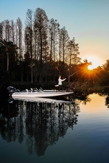 high school senior fisherman on bass boat fishing on a lake at sunrise with off camera lighting