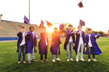 high school seniors in cap and gowns posing on school soccer field