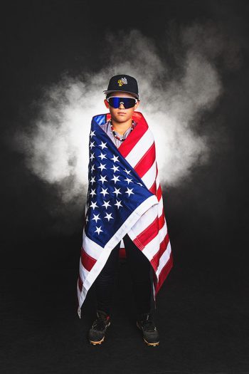 Young baseball player wrapped in an american flag in a studio setting in bartow, florida using dramatic lighting and smoke