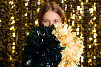 Portrait of Cheerleader holding poms in front of a shimmer wall, one of BC Visuals signature backgrounds.