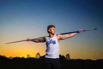 high school senior track and field athlete holding a javelin in front of a sunset sky