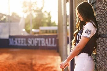 high school softball player leaning up against the dugout at sunset with natural light